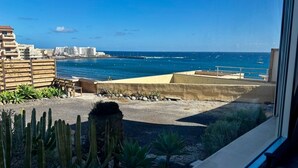 A coastal view from a balcony with a clear sky, a sandy beach, and a row of buildings in the background.