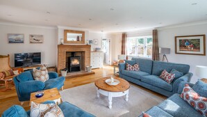 A spacious living room with a fireplace, blue sofas, a television, and a dining area. - Waterside, Wiveton, Norfolk (Wiveton)