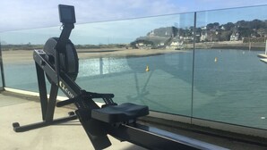 A rowing machine on a balcony overlooking a beach with houses in the background. - Family Gite in the Countryside, with Outdoor Heated Swimming Pool. Pet Friendly (Montsenelle)
