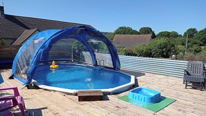 An outdoor swimming pool with a blue cover, surrounded by a wooden deck. - Family Gite in the Countryside, with Outdoor Heated Swimming Pool. Pet Friendly (Montsenelle)