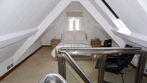 Une chambre aménagée dans les combles, avec un lit, deux tables de chevet, une chaise et une fenêtre de toit.