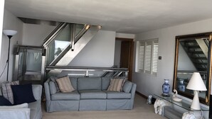 Un salon moderne avec un canapé gris, une table basse en verre et un escalier menant à un niveau supérieur.