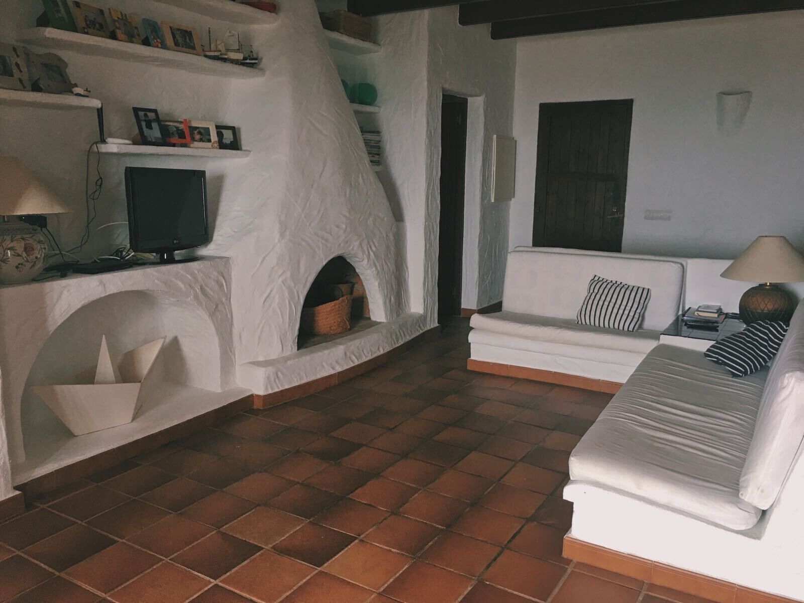 Een woonkamer met een witte bank, een televisie, een open haard en een betegelde vloer.