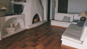 Ein Wohnzimmer mit weißem Sofa, Fernseher, Kamin und Fliesenboden.