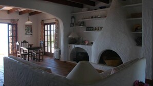 Ein gemütliches Wohnzimmer mit Kamin, Holzbalken und einem Essbereich mit Tisch und Stühlen.