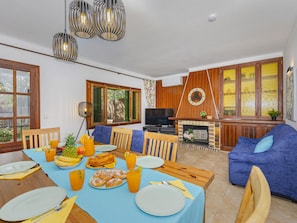 A spacious living area with a dining table set for a meal, a television, and a fireplace.