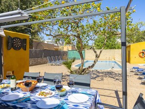 An outdoor dining area with a pool, a table set for a meal, and a dartboard.