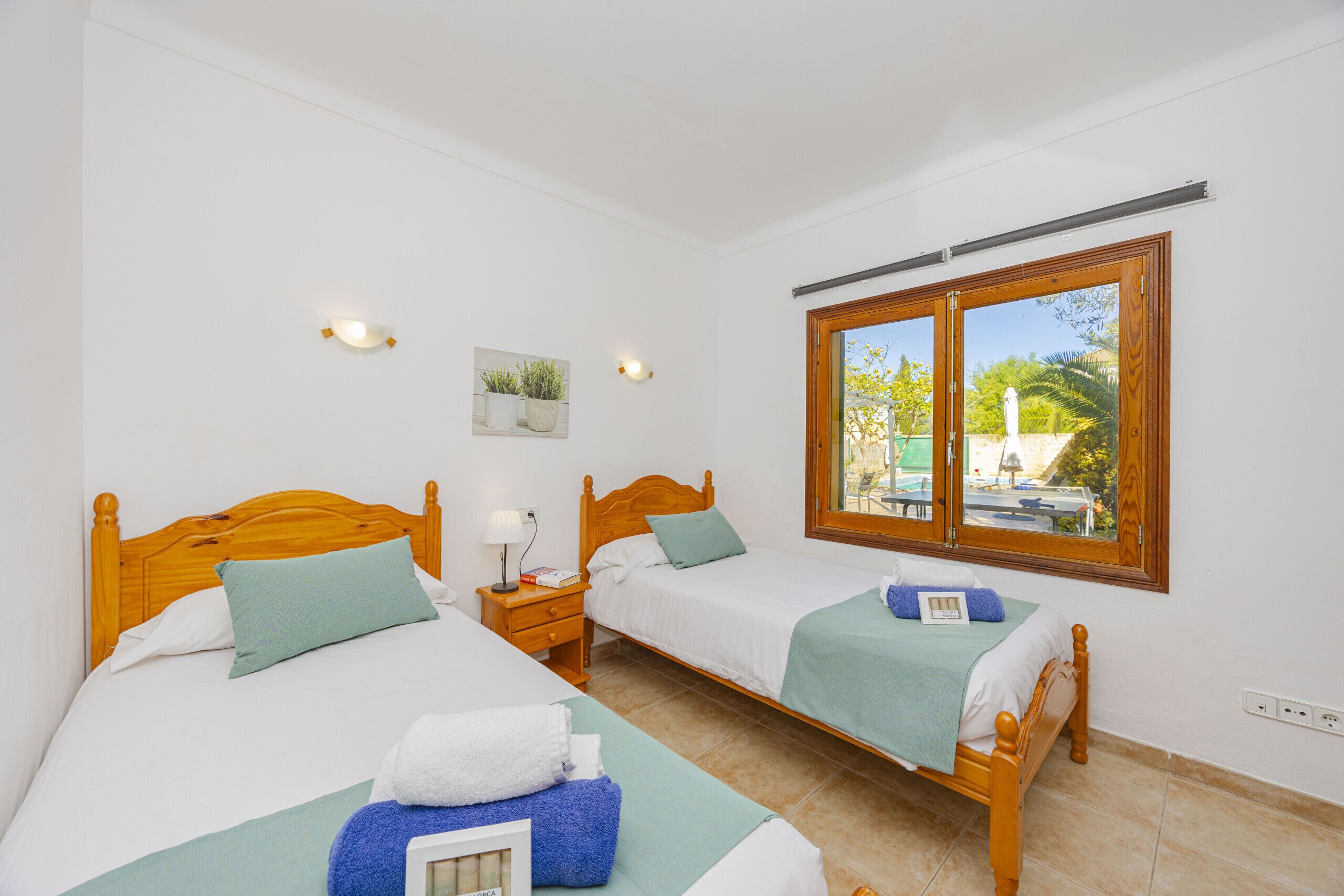 Une chambre avec deux lits en bois, une fenêtre donnant sur un beau paysage et un luminaire fixé au mur.