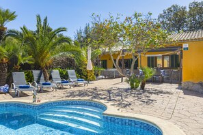 Un espace piscine comprenant des chaises longues, une petite piscine et un bâtiment jaune avec un toit en tuiles.