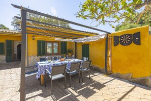 Un patio con una mesa lista para comer, una pérgola y un dardo colgado en una pared amarilla.