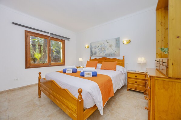 Une chambre à coucher avec un lit en bois, une table de chevet, une commode, une fenêtre avec des stores et un tableau accroché au mur.