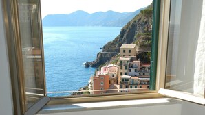 Una habitación con vista al mar y edificios, una mesa con un plato de conchas marinas, y una ventana con vista al mar.