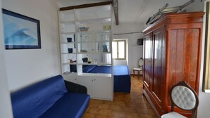 Una habitación con un sofá azul, un armario de madera y una estantería con varios objetos.