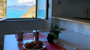 Una cocina con vista al mar, una mesa de comedor con un plato de cruasanes, una cafetera y una taza.