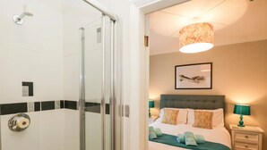 A hotel room with a glass shower enclosure, a bed with a green bedspread, two bedside lamps, and a framed artwork on the wall. - Windermere house with Lake View, 3 bed 3 bath, dog friendly with ample parking (Bowness-on-Windermere)