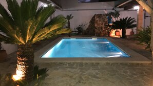 Et rektangulært swimmingpool med en stenkant, omgivet af krukker med planter og palmer.