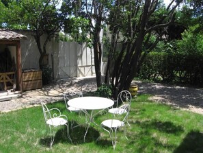 Une terrasse avec une table ronde et quatre chaises, entourée d’arbres et d’une clôture blanche.