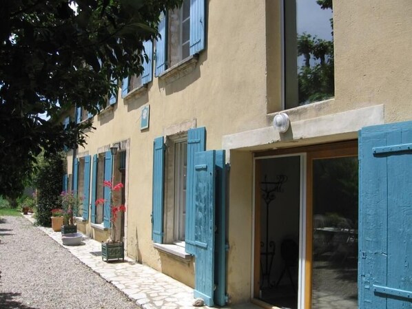 Un bâtiment avec des volets bleus, un chemin de pierre et des plantes en pot.