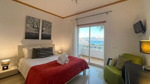 Una camera d'albergo con un letto, una coperta rossa, una sedia verde, una televisione e un balcone con vista.