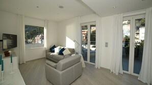Un salon moderne avec un canapé, un téléviseur à écran plat et un balcon doté de portes vitrées.