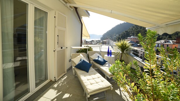 Un balcon avec deux chaises longues, une table ornée de bouteilles bleues et une vue sur une colline.