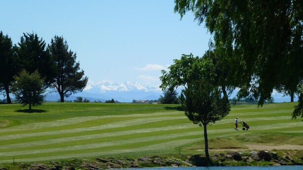 Un parcours de golf avec un plan d’eau au premier plan, des arbres et une chaîne de montagnes en arrière-plan.