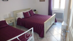 Une chambre avec deux lits, une table de chevet, une commode et une fenêtre avec des rideaux.