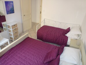 A bedroom with two beds, a white dresser, and a wicker storage unit. - Well-equipped House At Foot of Medieval Cité with Garage, Wifi & 2 Shower rooms (Carcassonne)