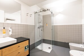 Et moderne badeværelse med bruseniche, hvid vask og separat toiletområde.
