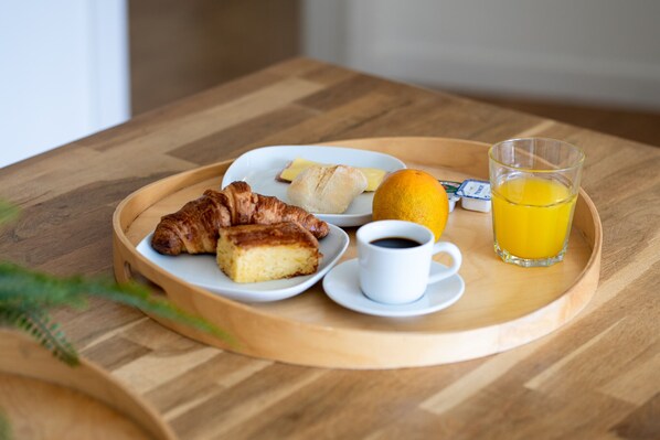 En bakke med morgenmad: croissanter, et stykke ost, en citron, et glas appelsinjuice og en kop kaffe på et træbord.