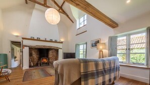 A cozy room with a fireplace, a bed with a plaid blanket, wooden floors, and a window with a view of greenery. - Field Row, Field Dalling, Norfolk (Holt)