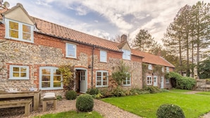 A stone and brick house with a tiled roof, a garden with a gravel path, and a wooden bench. - Field Row, Field Dalling, Norfolk (Holt)