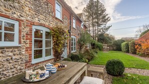 A stone and brick building with a wooden table set with tea and pastries, surrounded by a well-maintained garden. - Field Row, Field Dalling, Norfolk (Holt)