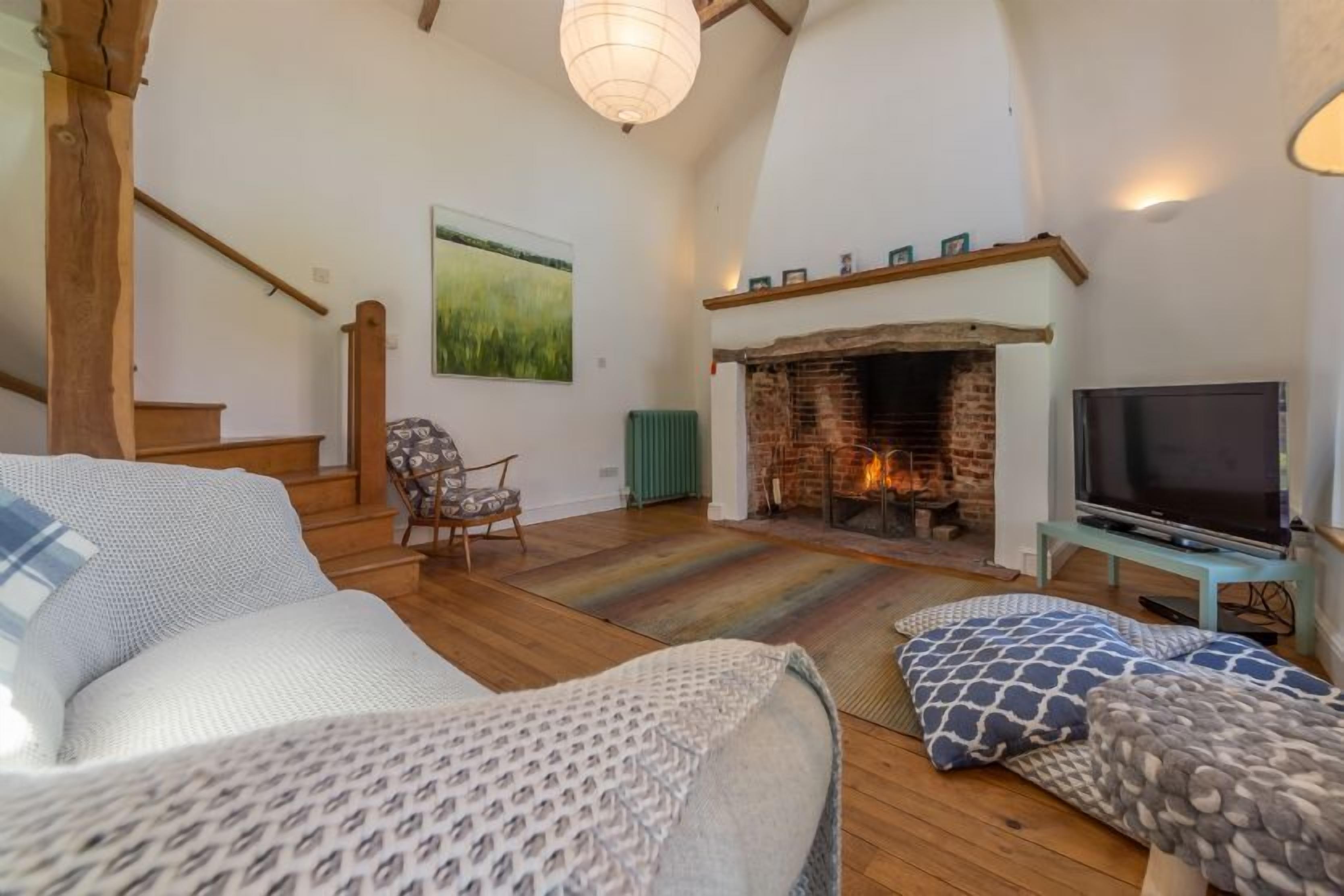 A cozy living room with a fireplace, wooden flooring, a TV, and a staircase.
