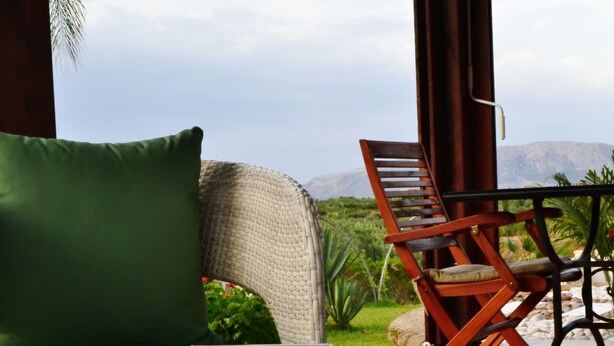 Una habitación con vista a montañas, un sofá verde, una silla de madera y una mesa con libros y una decoración de flor de loto.