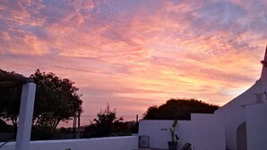 Solnedgang over en hvid bygning med have og et hegn.