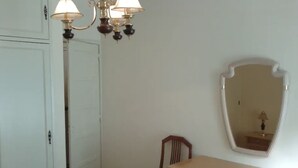 Ein Schlafzimmer mit einer weißen Tür, einer Holzkommode mit Schubladen, einem Stuhl und einem Spiegel an der Wand.