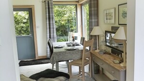 Een eetgedeelte met een tafel voor twee personen, een stoel, een lamp en een spiegel op een houten dressoir.