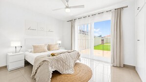 Een slaapkamer met een bed, nachtkastjes, een plafondventilator en uitzicht op een groen gazon.