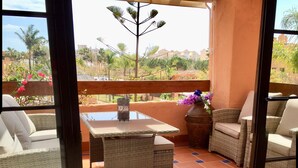 A balcony with wicker furniture, a table, and a vase of flowers. - Stylish Luxury Apartment, Stunning Pool and Gardens, Secluded Beach (Estepona)