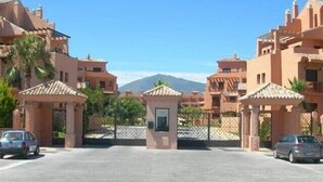 A gated entrance to a residential area with multiple buildings, a clear sky, and a mountain in the background. - Stylish Luxury Apartment, Stunning Pool and Gardens, Secluded Beach (Estepona)
