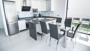 A modern kitchen with a central island, stainless steel appliances, and a dining area with glass tables and chairs. - Luxury 6-person villa with swimming pool, sunroof near the beach and golf courses (San Pedro del Pinatar)
