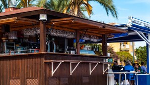 A wooden outdoor bar with a covered seating area, a counter with glassware, and a blue awning. - Luxury 6-person villa with swimming pool, sunroof near the beach and golf courses (San Pedro del Pinatar)