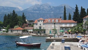A waterfront hotel with stone buildings, a dock with a boat, and mountains in the background. - LUXURY VILLA WITH PRIVATE POOL ON BEAUTIFUL AND ACCESSIBLE LUSTICA PENINSULA (Ðuraševici)