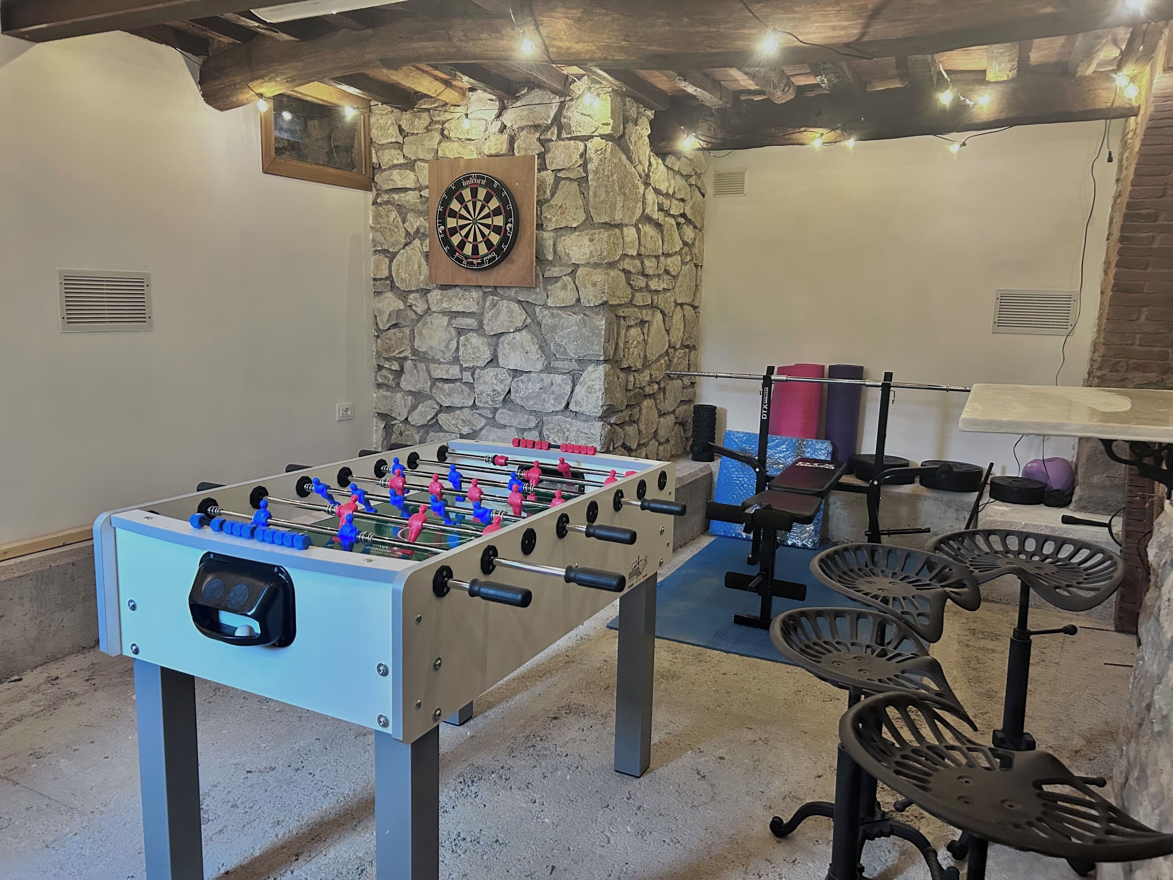 Een tafelvoetbaltafel in een kamer met stenen muren en een dartbord.