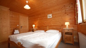 A wooden room with a double bed, two bedside tables with lamps, a radiator, and a wooden wardrobe.