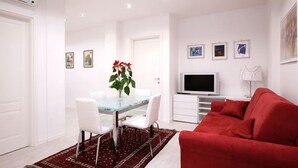 A modern living room with a red sofa, a glass dining table with white chairs, a TV, and framed artwork on the wall. - Luxury apartment 200 meters from St. Peter's basilica, in the heart of Rome (Roma)