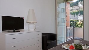 A modern room with a flat-screen TV on a white dresser, a white lamp, a black chair, and a balcony with a glass door. - Luxury apartment 200 meters from St. Peter's basilica, in the heart of Rome (Roma)
