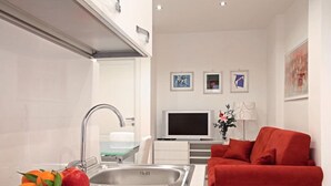 A modern kitchen with a stainless steel sink, a dining table with a plate of fruit, a red sofa, and a flat-screen TV in a living area. - Luxury apartment 200 meters from St. Peter's basilica, in the heart of Rome (Roma)
