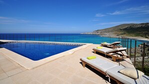 Une piscine avec vue sur la mer et une terrasse en bois équipée de chaises longues.